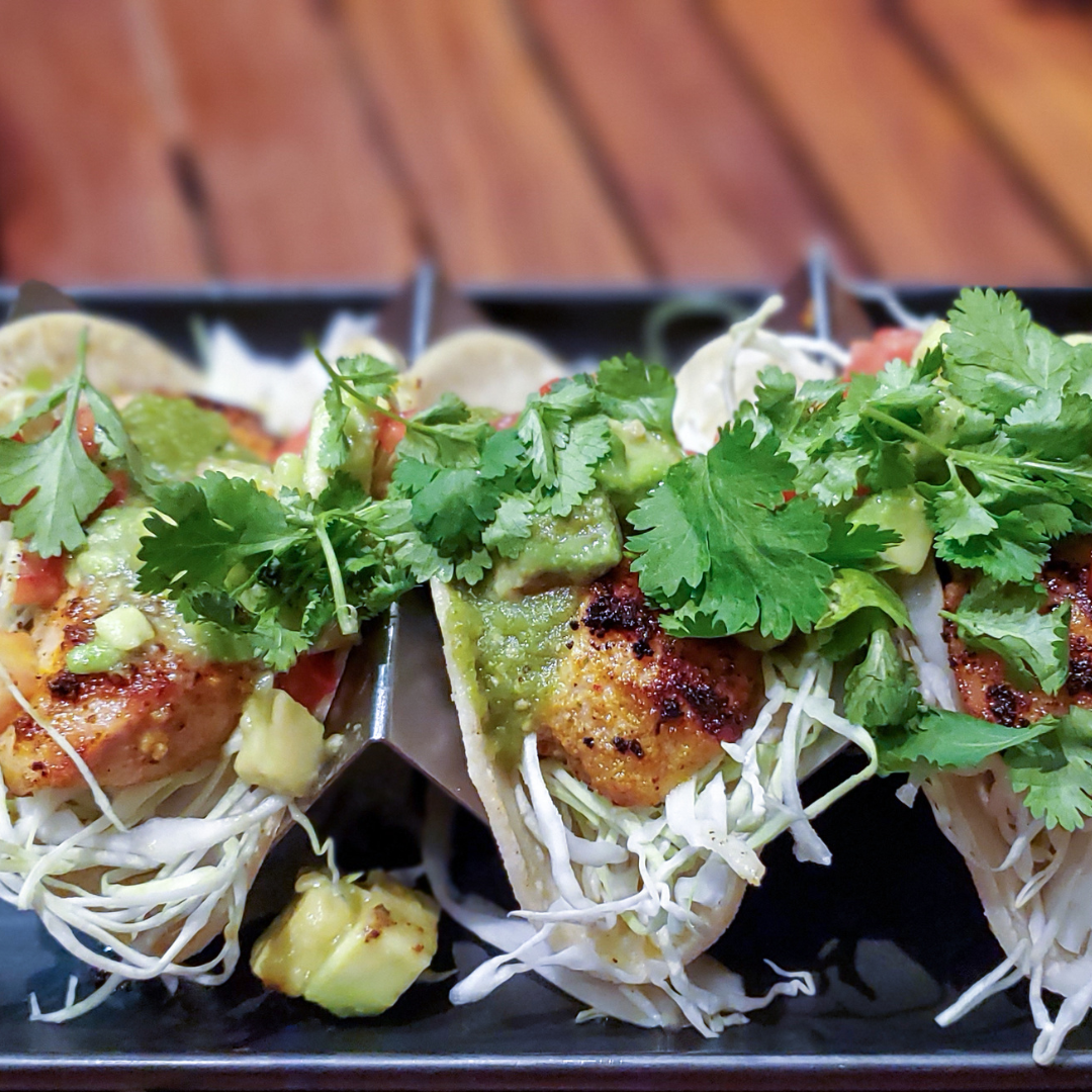 A tray of 3 fish tacos with cilantro covering them